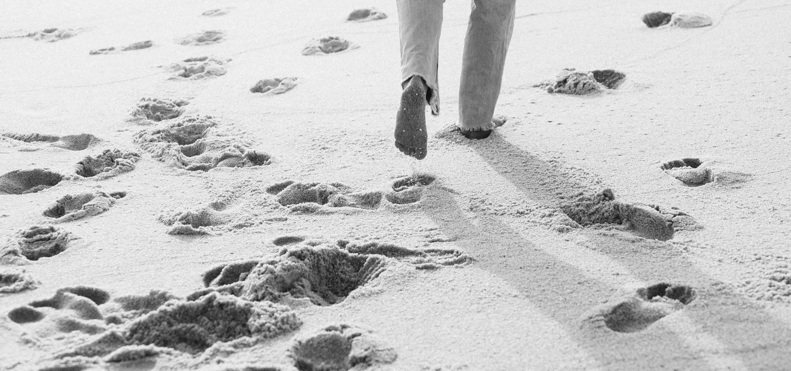 Person walking barefoot on sand with footprints behind