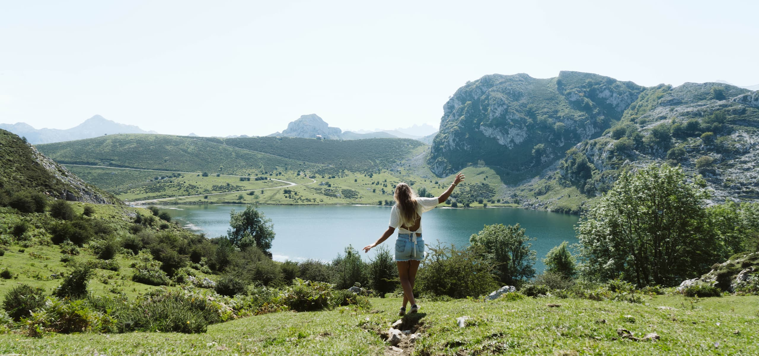 Persona de pie junto a un lago rodeado de colinas verdes y montañas en Cantabria, España