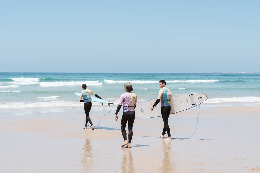 Surf instructors walking across the beach with boards in Alentejo Portugal
