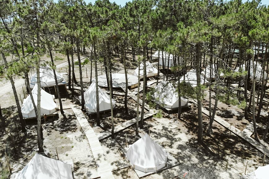 Aerial view of white bell tents and wooden paths in the Dreamsea Portugal Centro pine forest camp