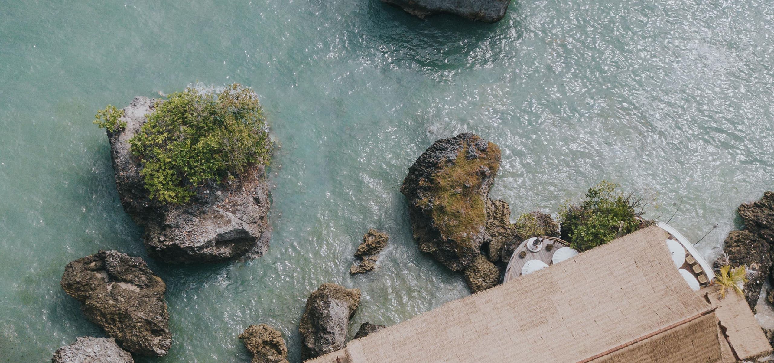 Aerial view of turquoise ocean and limestone rocks beside a clifftop surf camp in Uluwatu, Bali