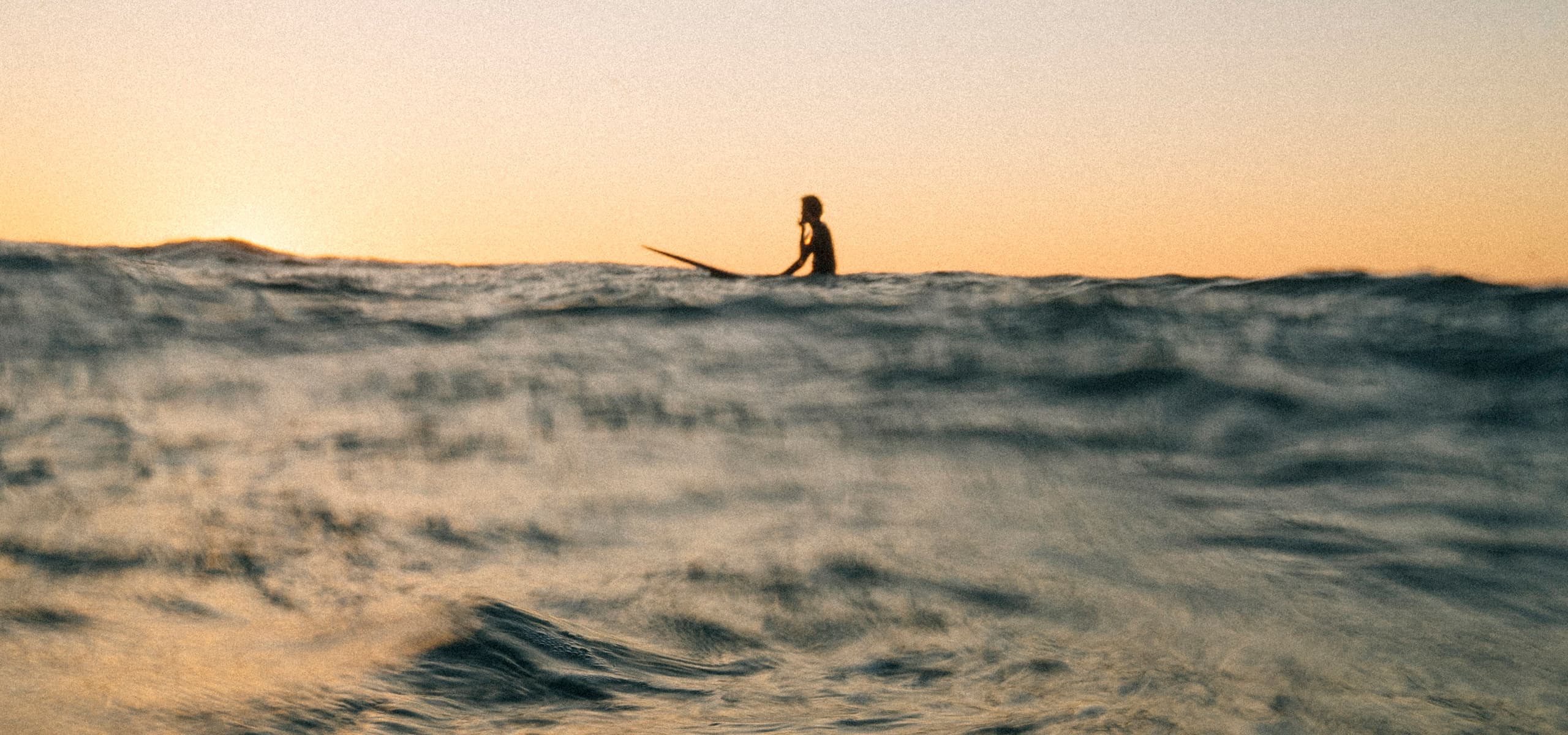 Silhouette of a surfer sitting on a board in the ocean at sunset in Imsouane, Morocco