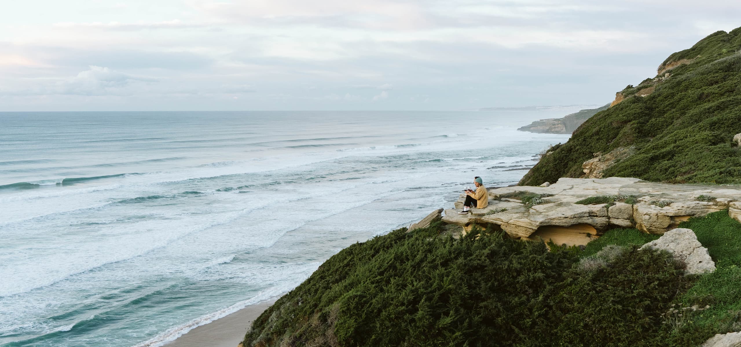 Person sitting on a rocky cliff overlooking the Atlantic Ocean near Sintra, Portugal