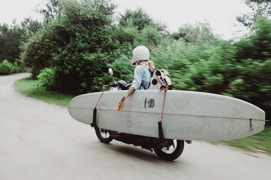Guest riding a scooter with a surfboard through Bali