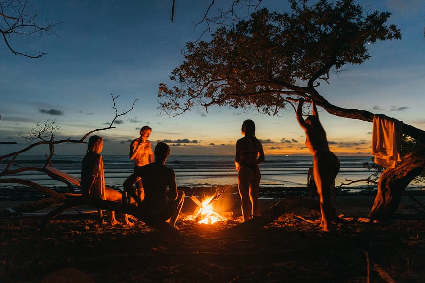 Guests gathered around a beach bonfire at sunset in Playa Avellanas