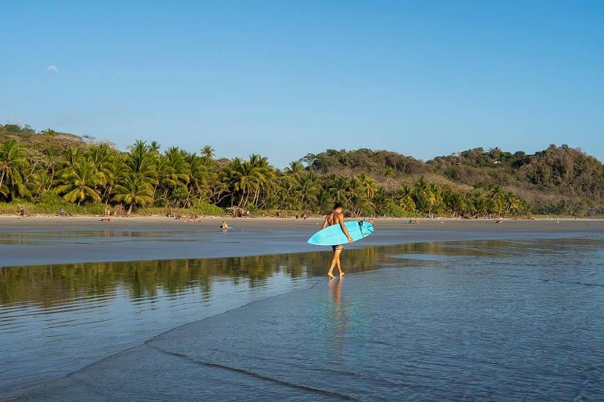 Surfer walking along Playa Hermosa Santa Teresa with a blue surfboard