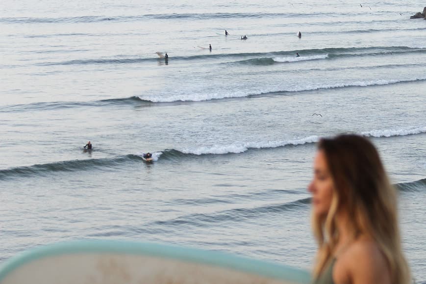 Guest with surfboard overlooking surfers in Imsouane Bay