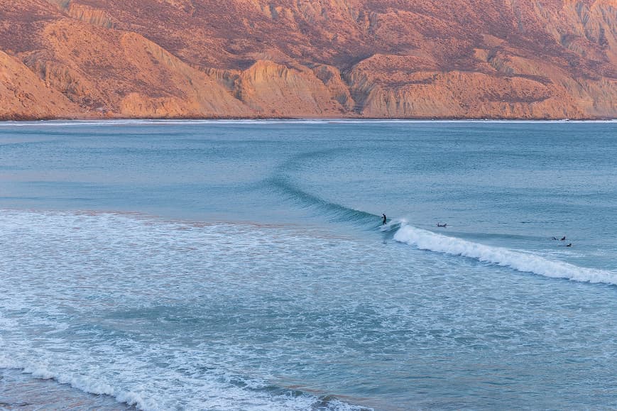 Surfer riding a long wave in Imsouane Bay with Moroccan cliffs in the background