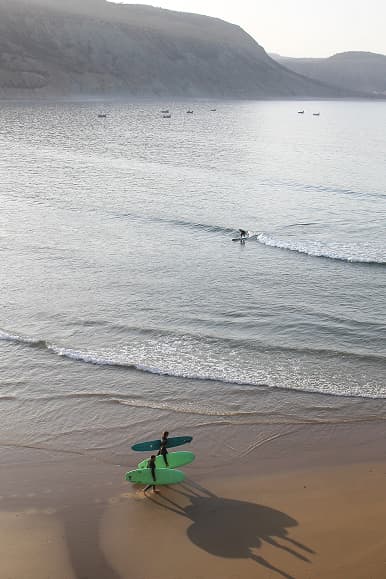 Surfer riding a small wave while other surfers carry boards on Imsouane beach