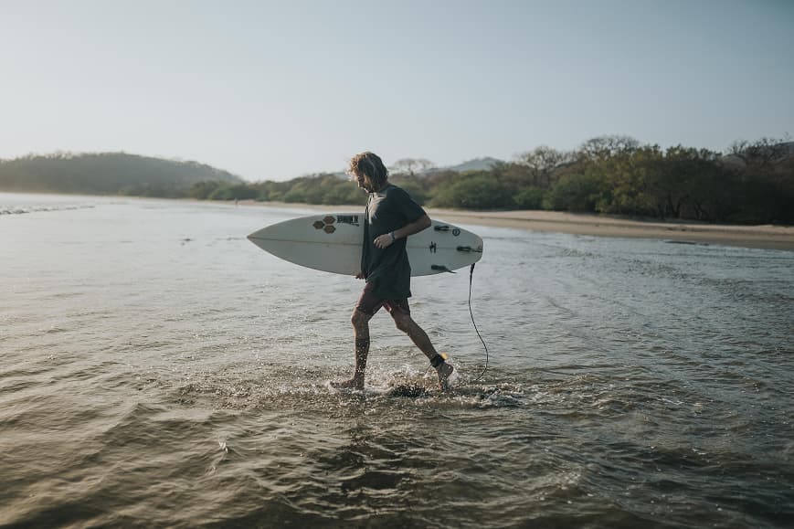 Surfer walking through shallow water with a surfboard on the Pacific coast of Nicaragua