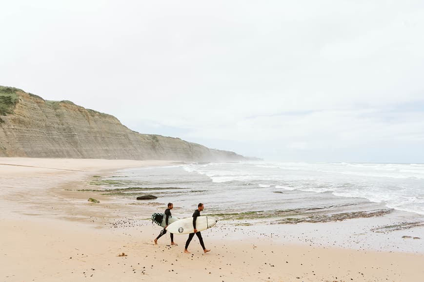 Two surfers walking along the beach with surfboards on the Sintra coast
