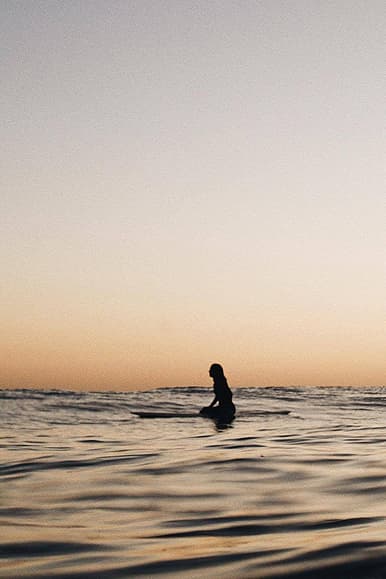Surfer sitting in the ocean at sunset in Portugal