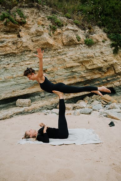 Two guests practicing partner acro yoga on the beach below the cliffs