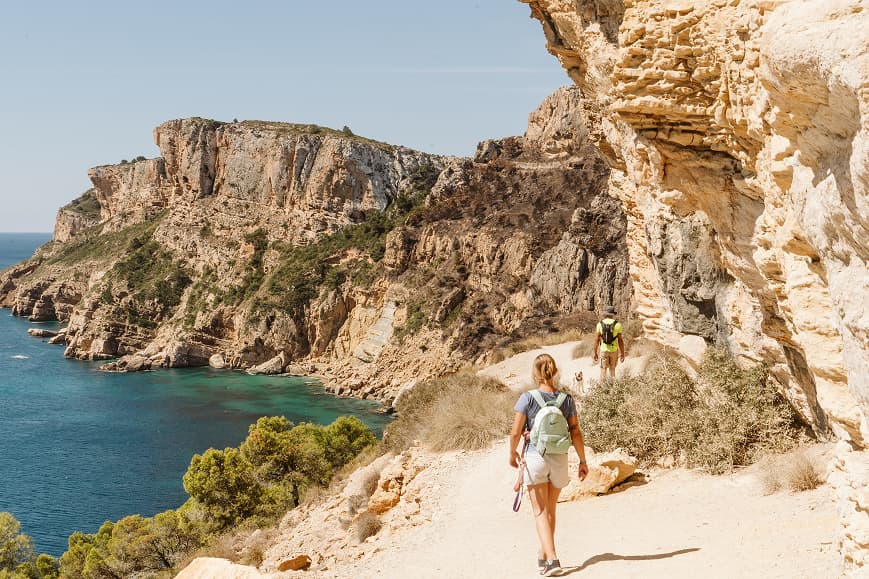Hikers walking along a cliffside trail above the Mediterranean Sea in AlicantePerson diving underwater in clear turquoise water near rocky Mediterranean cliffs
Guest paddleboarding below limestone cliffs on the Costa Blanca
Two guests kayaking inside a rocky sea cave with crystal-clear Mediterranean water