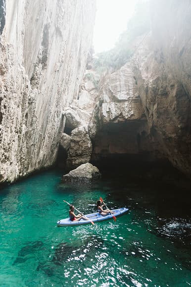Two guests kayaking inside a rocky sea cave with crystal-clear Mediterranean water