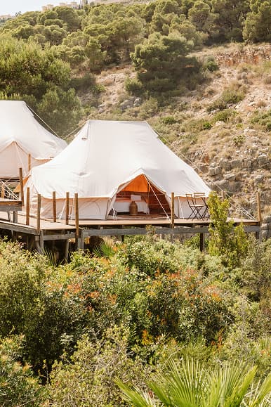 White glamping tents with wooden terraces surrounded by Mediterranean vegetation