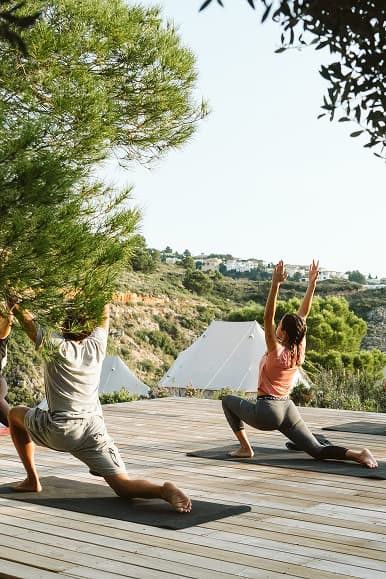 Guests stretching during an outdoor yoga class surrounded by tents and pine trees