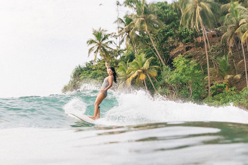 Surfer riding a wave in front of tropical cliffs and palm trees in Sri Lanka