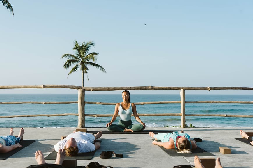 Yoga class relaxing on mats with the ocean and palm trees in the background