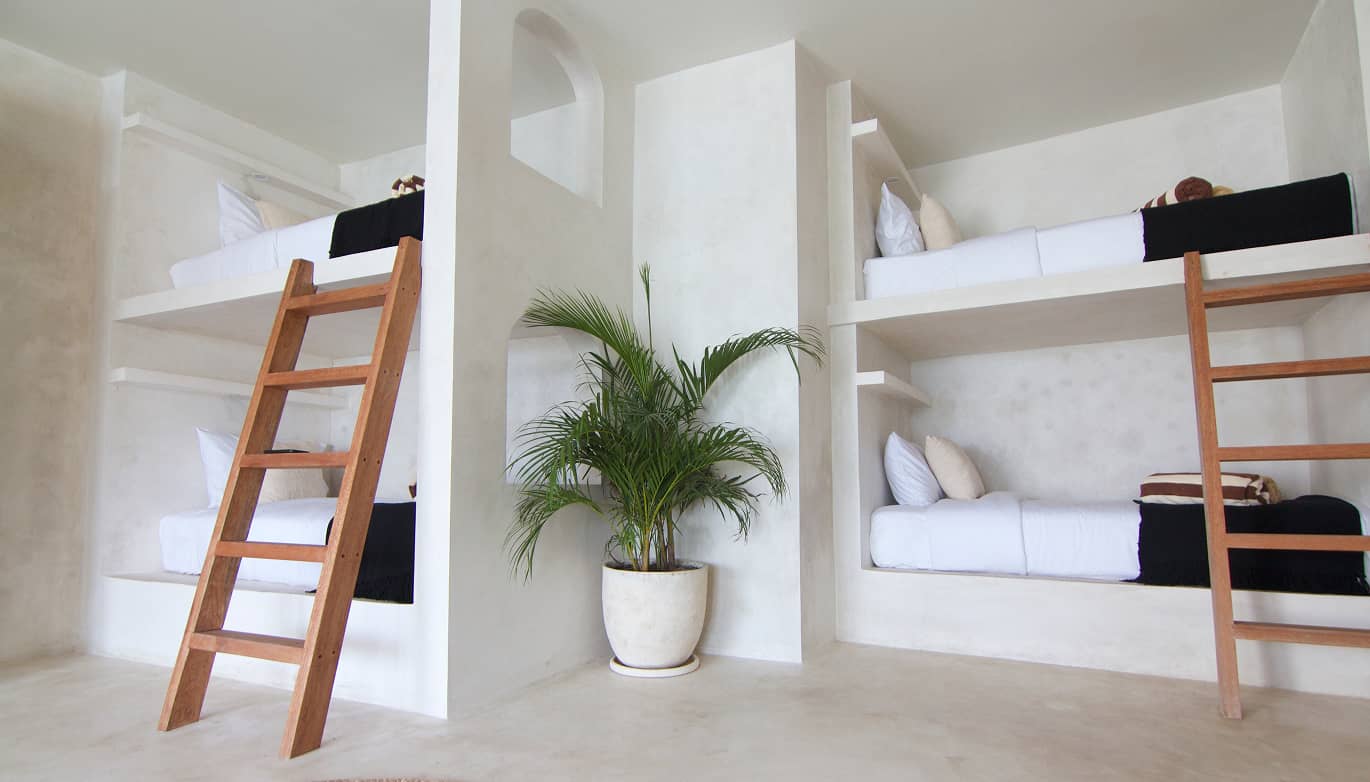 Shared room at Dreamsea Lombok with white built-in bunk beds, wooden ladders and a potted palm